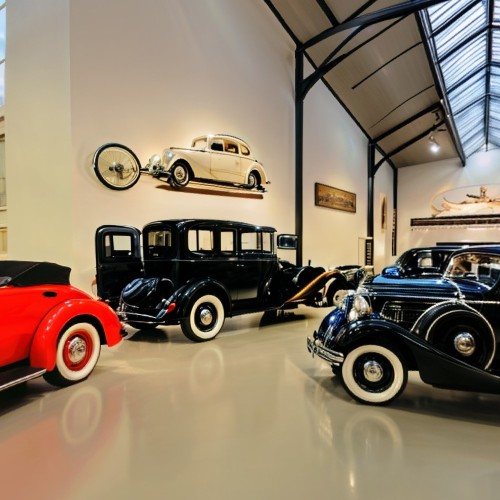 Vintage Car Museum with Classic Automobiles: A spacious exhibition hall filled with vintage cars from various decades, each in pristine condition. The polished cars are arranged in rows, with informational plaques detailing their history, while soft lighting enhances their shiny exteriors.