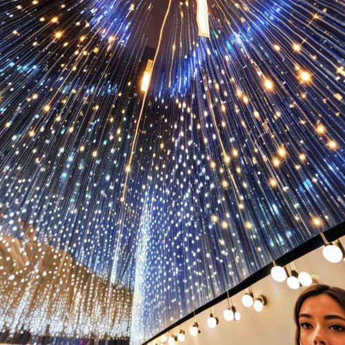 Art Installation with Hanging Lights and Mirrors: An immersive art installation featuring hundreds of small lights hanging from the ceiling and mirrored walls that reflect the lights endlessly. The room has a magical, otherworldly atmosphere, as visitors feel like they are walking through a sea of stars.